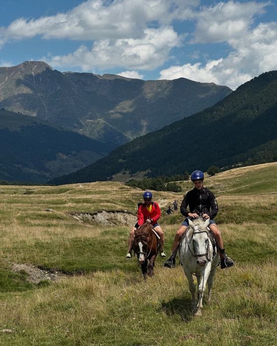 Dos jinetes por un prado con montañas al fondo